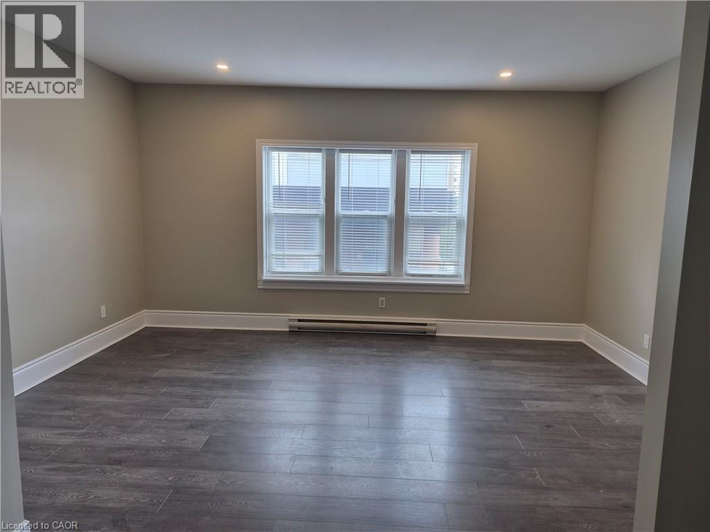 Spacious room featuring wood-finish flooring, recessed ceiling lighting, and a triple window off of kitchen - 181 King Street E Unit# 2, Kitchener, ON
