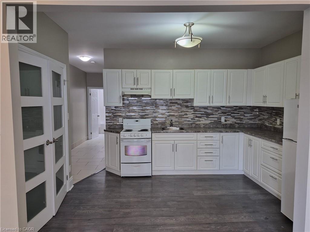 Kitchen featuring white cabinetry, a mosaic tile backsplash, dark countertops, and wood-finish flooring - 181 King Street E Unit# 2, Kitchener, ON