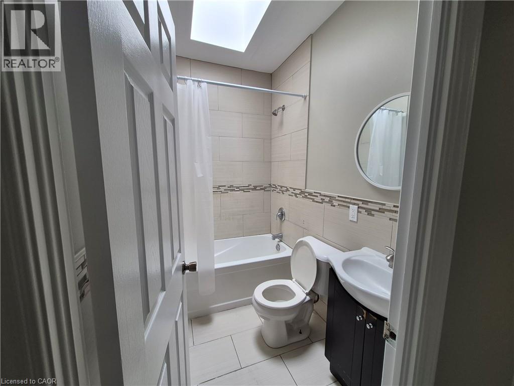 Bathroom featuring a skylight, tile flooring, bathtub with tile surround, mosaic accent tile, and a dark wood-finish vanity with an integrated sink - 181 King Street E Unit# 2, Kitchener, ON