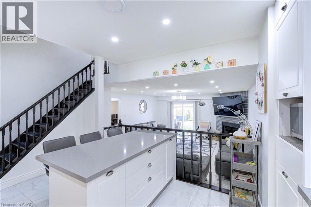 Modern kitchen island featuring a light-toned countertop, white cabinetry with hardware, and seating for three - 214 Merrilee Crescent, Hamilton, ON