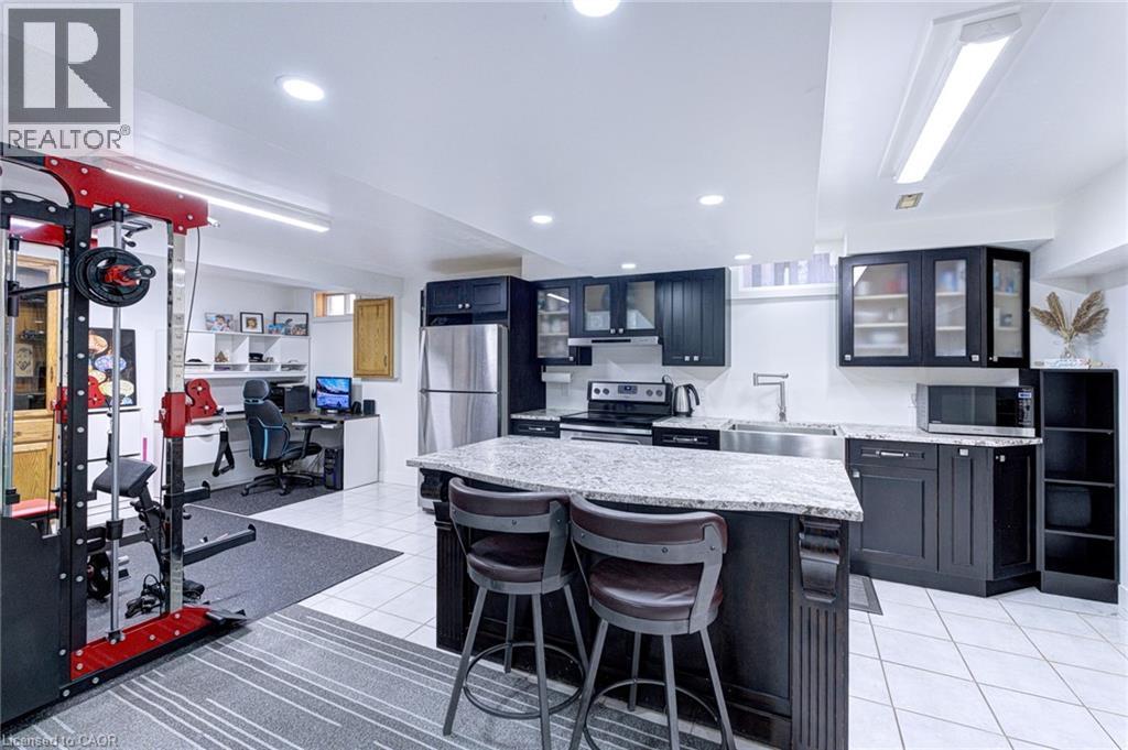 Open-concept lower level featuring a full kitchen with dark cabinetry, stainless steel appliances, and a granite island with seating - 214 Merrilee Crescent, Hamilton, ON