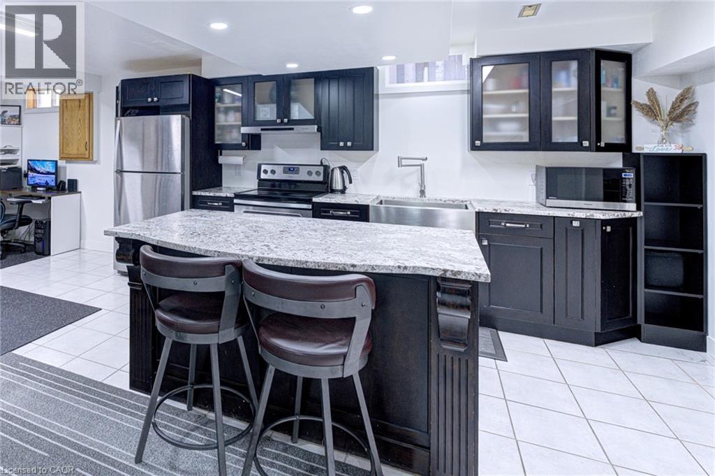 Kitchen featuring dark wood cabinetry, light granite countertops, stainless steel appliances, and white tile flooring - 214 Merrilee Crescent, Hamilton, ON