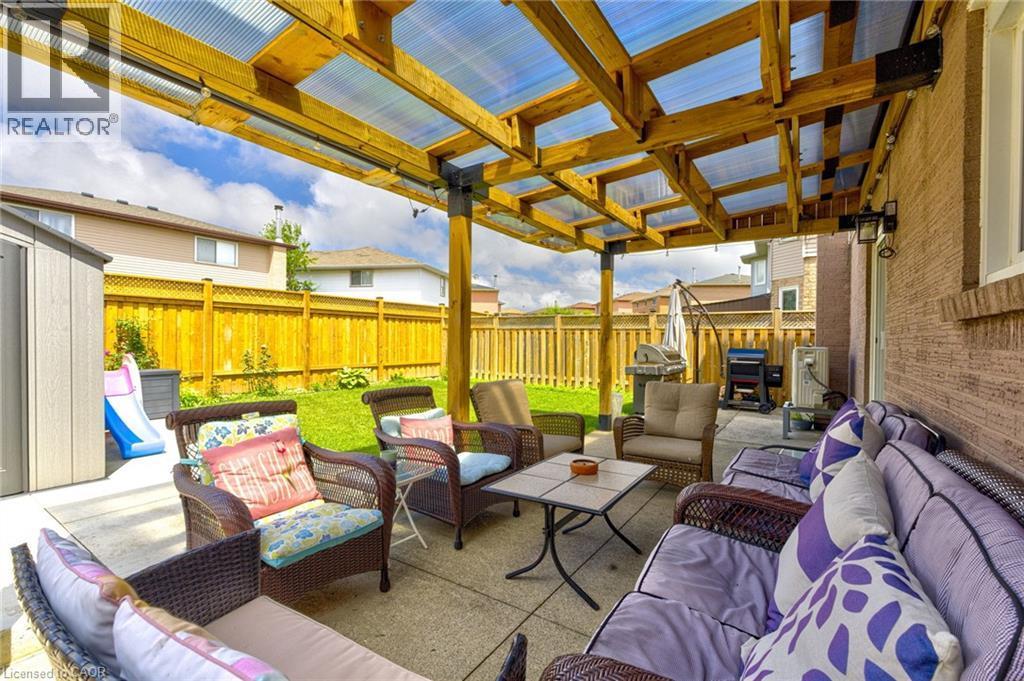 Paved patio area featuring a clear corrugated roof, wooden pergola structure, and brick exterior wall - 214 Merrilee Crescent, Hamilton, ON