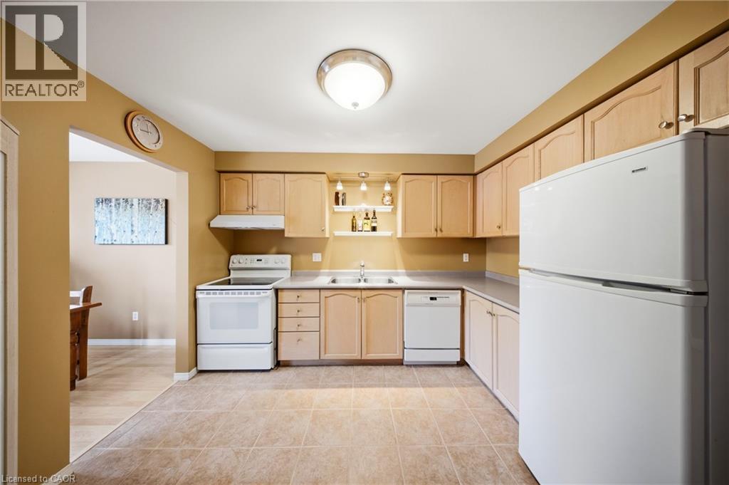 Kitchen featuring light wood-finish cabinetry, white appliances, and tiled flooring - 16 Scottacres Boulevard, Caledonia, ON