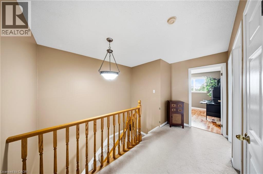 Upper-level landing featuring neutral carpet flooring, a natural wood-finish staircase railing, and a bronze-finish pendant light fixture - 16 Scottacres Boulevard, Caledonia, ON