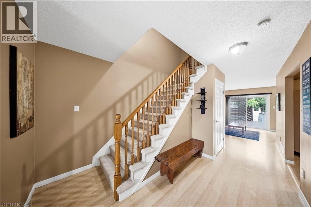 Foyer featuring light wood-finish flooring, staircase with carpeted treads and wood railing, and neutral wall tones - 16 Scottacres Boulevard, Caledonia, ON