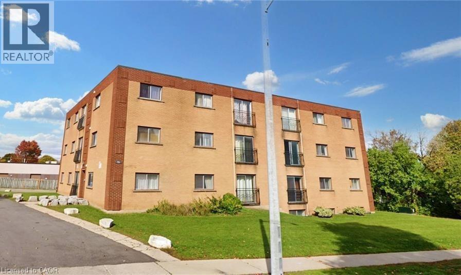 Four-story brick building featuring multiple balconies with black railings, individual windows, and a surrounding green lawn - 76 Brybeck Crescent Unit# 302, Kitchener, ON