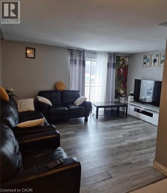 Living area featuring wood-finish flooring, neutral wall tones, and a sliding glass door with balcony access - 76 Brybeck Crescent Unit# 302, Kitchener, ON