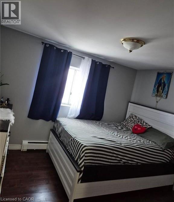 Room with wood-finish flooring, a window with dark and sheer curtains, a baseboard heater, and a flush-mount ceiling light fixture - 76 Brybeck Crescent Unit# 302, Kitchener, ON