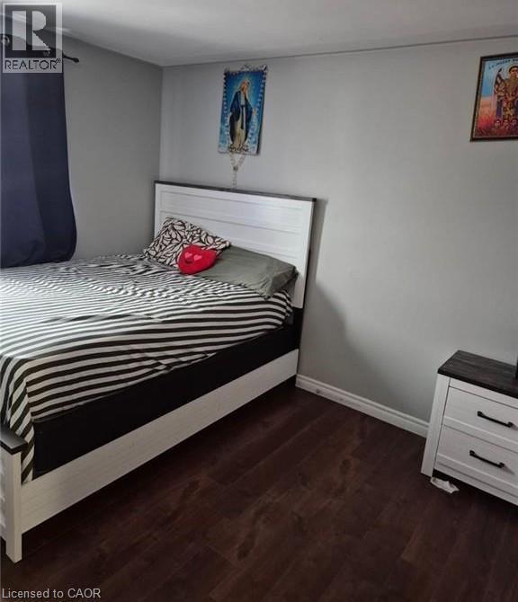 Room featuring wood-finish flooring, light grey painted walls, white baseboards, and a window with a dark curtain - 76 Brybeck Crescent Unit# 302, Kitchener, ON