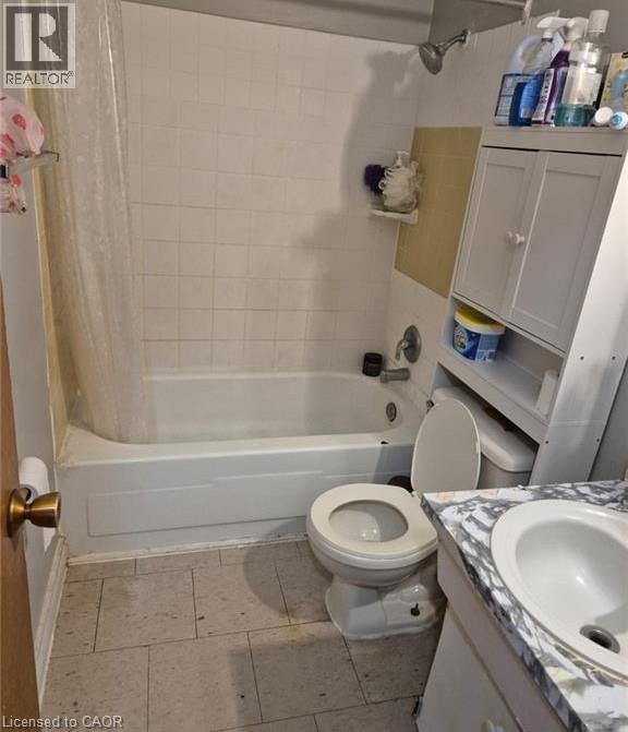 White bathtub with shower, white square tile surround, white toilet, and a vanity with a circular sink and a stone-finish countertop - 76 Brybeck Crescent Unit# 302, Kitchener, ON
