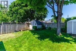 Expansive backyard featuring a manicured lawn, mature trees, a wooden privacy fence, and two storage sheds - 