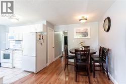 Kitchen and dining area featuring white cabinetry, white appliances, wood-finish flooring, and a ceiling-mounted light fixture - 
