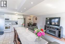 Kitchen and living area featuring white cabinetry, light-toned countertops, recessed lighting, and tile flooring - 