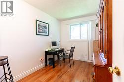 Light-filled room featuring wood-finish flooring, white walls, and a window with vertical blinds - 
