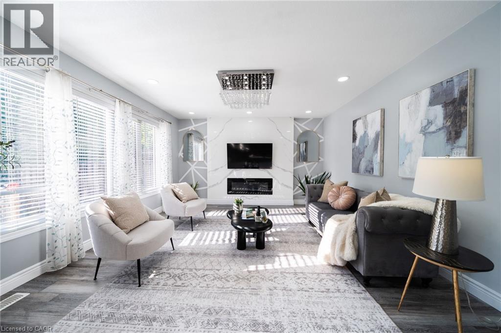 Bright living area featuring wood-finish flooring, a contemporary fireplace with a stone-look surround, and multiple windows with blinds - 151 Baldwin Drive, Cambridge, ON - Indoor Photo Showing Living Room With Fireplace