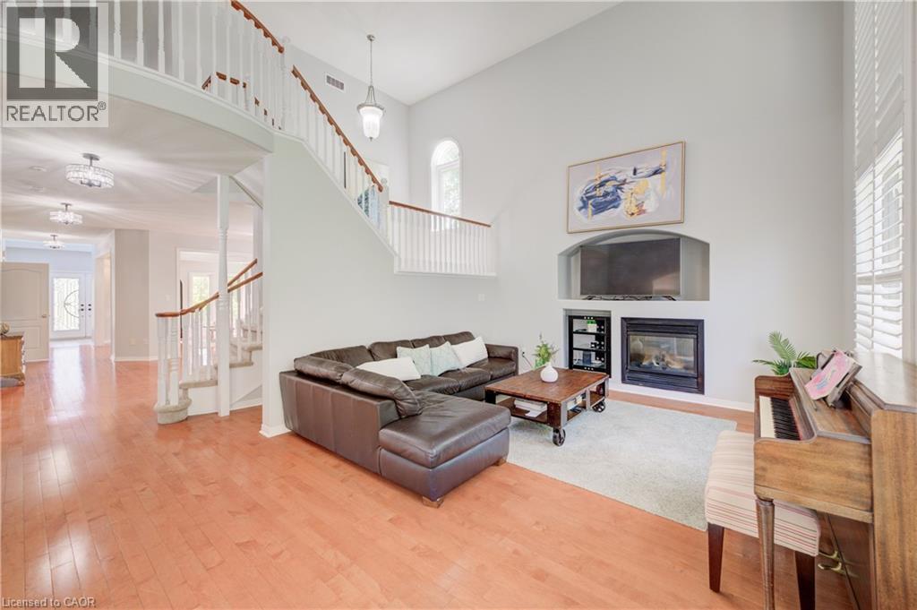 Vaulted living area featuring a fireplace with an integrated media niche, wood-finish flooring, a grand staircase with white balusters and wood handrails, and upper-level windows - 23 Buerkle Court, Kitchener, ON - Indoor Photo Showing Living Room With Fireplace