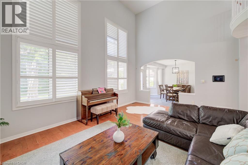Double-height living space featuring tall windows with plantation shutters, wood-finish flooring, an arched doorway, and an upper-level curved architectural detail - 23 Buerkle Court, Kitchener, ON - Indoor Photo Showing Living Room