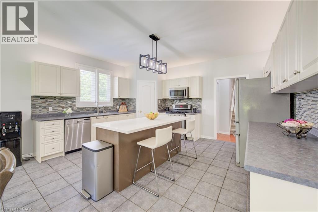Kitchen featuring a central island with countertop seating, white cabinetry, stainless steel appliances, and a mosaic tile backsplash - 23 Buerkle Court, Kitchener, ON - Indoor Photo Showing Kitchen