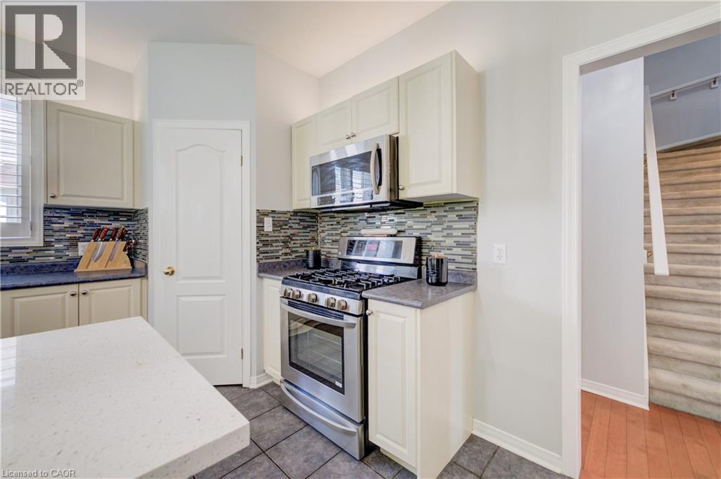 Kitchen featuring light-toned cabinetry, stainless steel appliances, a mosaic tile backsplash, and dark tile flooring - 23 Buerkle Court, Kitchener, ON - Indoor Photo Showing Kitchen