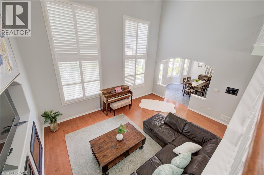 Living room featuring high ceilings, tall windows with white plantation shutters, wood-finish flooring, and an arched entry to the dining area - 23 Buerkle Court, Kitchener, ON - Indoor Photo Showing Other Room