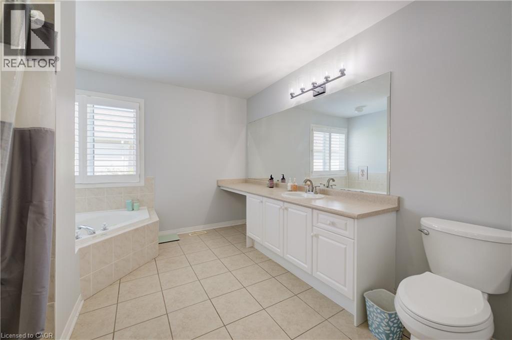 Bathroom featuring a corner soaking tub with tile surround, a spacious vanity with an integrated sink and light countertop, and a large wall-mounted mirror with overhead lighting - 23 Buerkle Court, Kitchener, ON - Indoor Photo Showing Bathroom