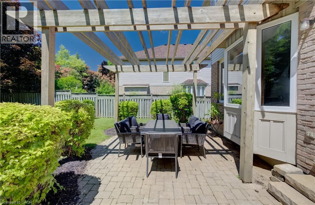 Pergola-covered patio featuring brick pavers, mature landscaping, wood fencing, and exterior brickwork - 23 Buerkle Court, Kitchener, ON - Outdoor