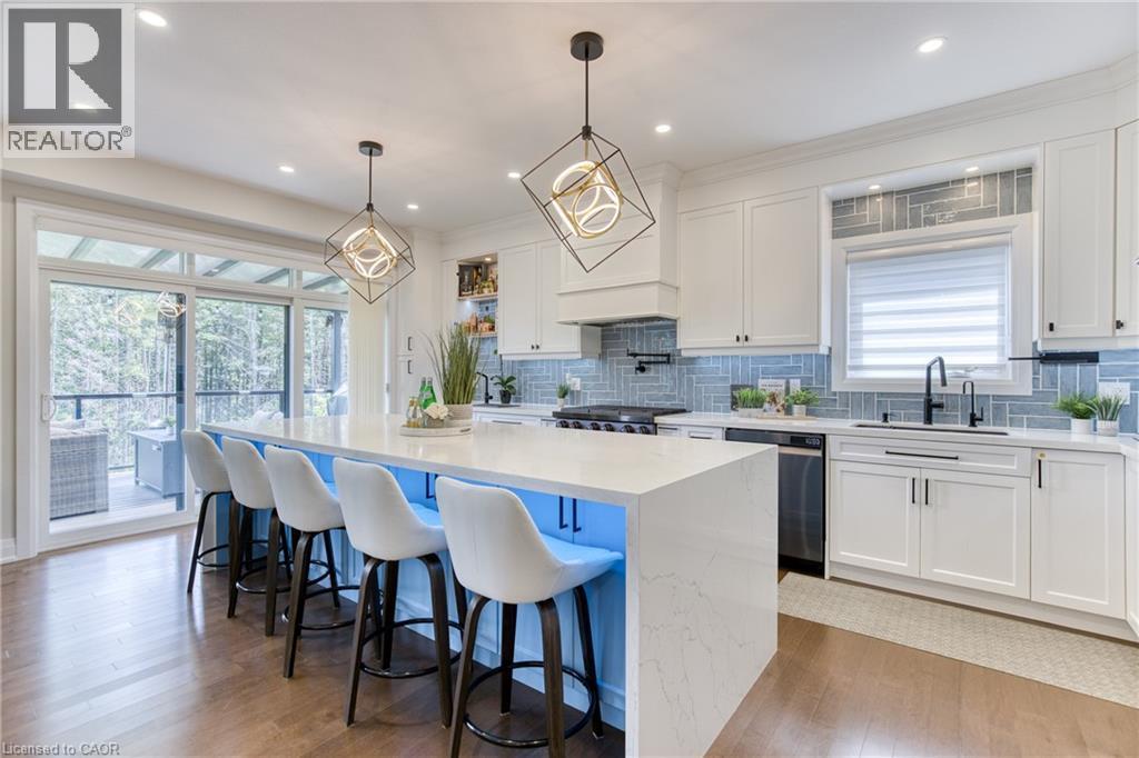 Spacious kitchen featuring a large central island with seating, white cabinetry, a light blue tiled backsplash, stainless steel appliances, and wood-finish flooring - 71 Ian Ormston Drive, Waterloo, ON