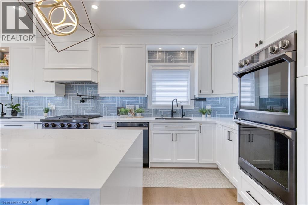 Kitchen featuring white shaker cabinetry, light blue herringbone tile backsplash, integrated stainless steel appliances, a center island with a light-toned countertop, and recessed lighting - 71 Ian Ormston Drive, Waterloo, ON