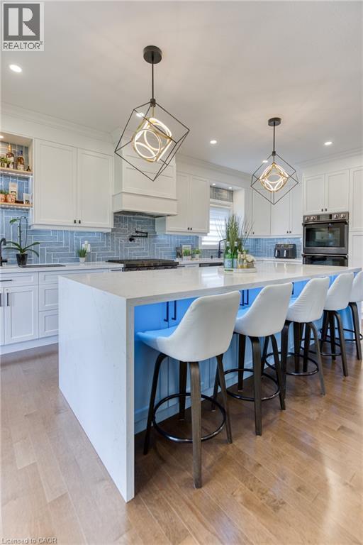 Kitchen featuring a large central island with seating, light wood-finish flooring, white cabinetry, a built-in oven, and a tile backsplash - 71 Ian Ormston Drive, Waterloo, ON