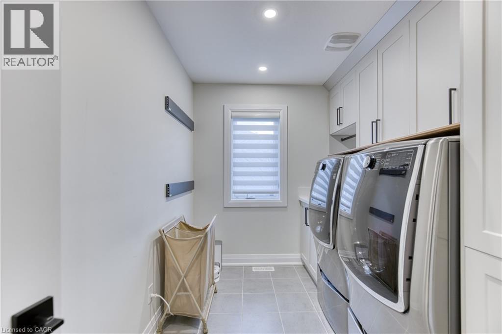 Dedicated laundry space featuring side-by-side front-load units, extensive white cabinetry with black hardware, a light-toned countertop, a window with privacy blinds, and recessed lighting - 71 Ian Ormston Drive, Waterloo, ON