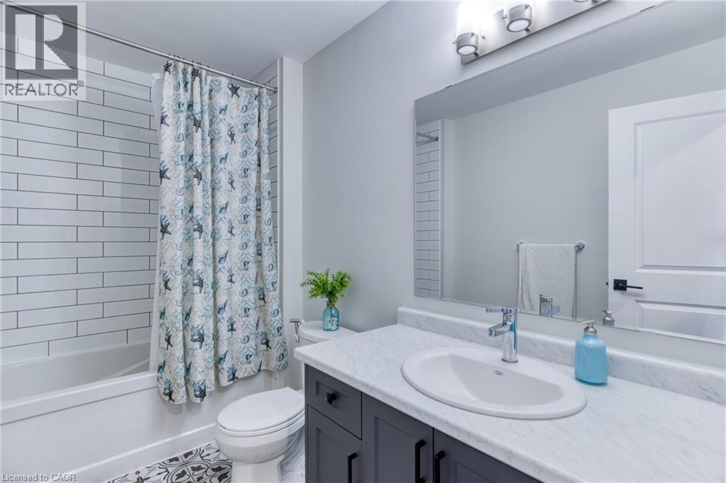 Bathroom featuring a white subway tile shower surround, a built-in tub, a dark wood-finish vanity with an integrated sink and light countertop, and patterned floor tile - 71 Ian Ormston Drive, Waterloo, ON