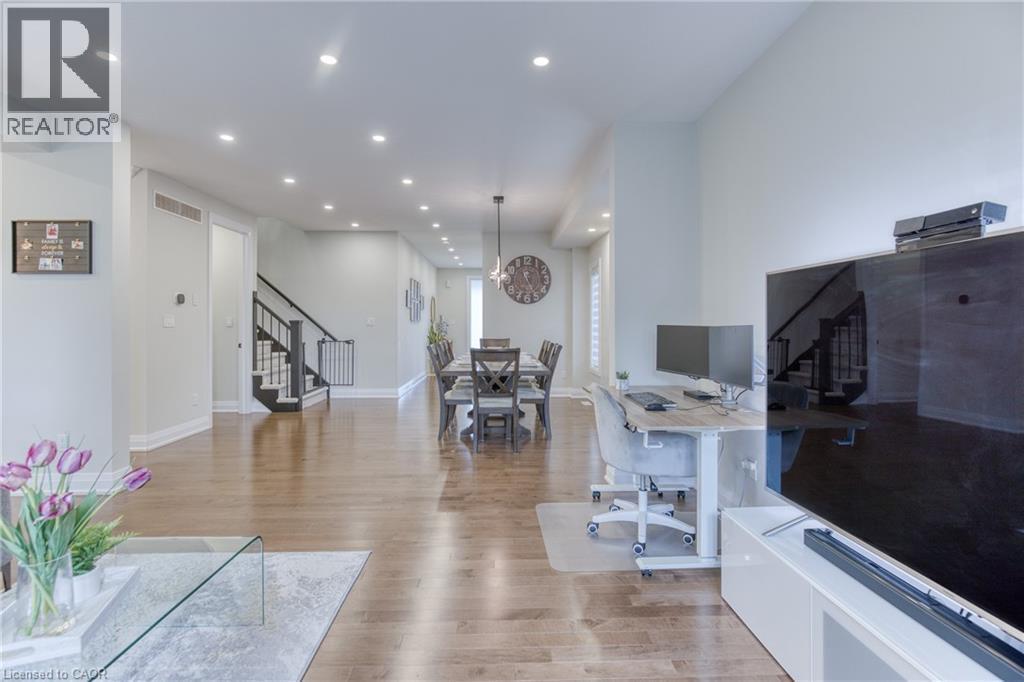 Expansive open-concept living area featuring wood-finish flooring, recessed lighting, and a staircase with dark wood treads and a black railing system - 71 Ian Ormston Drive, Kitchener, ON - Indoor