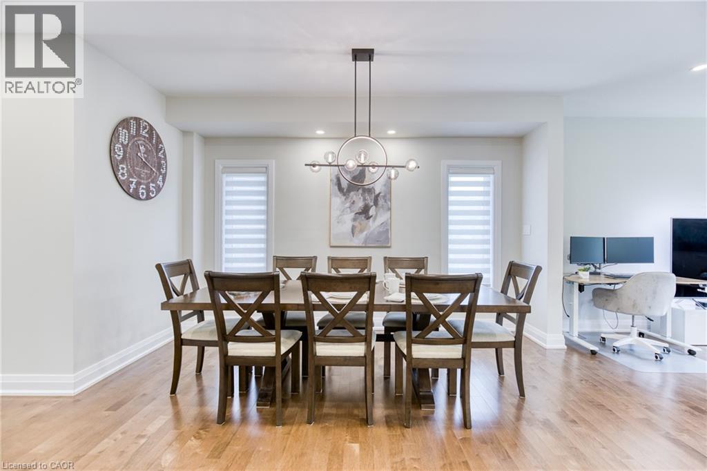 Formal dining space featuring wood-finish flooring, a modern linear chandelier, and two windows with horizontal blinds - 71 Ian Ormston Drive, Waterloo, ON