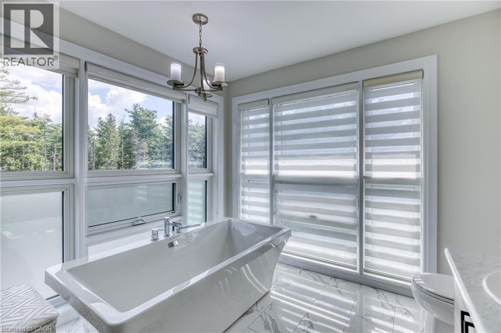 Freestanding soaking tub featuring chrome fixtures, surrounded by large windows with horizontal blinds, polished tile flooring, and a contemporary chandelier - 71 Ian Ormston Drive, Kitchener, ON - Indoor