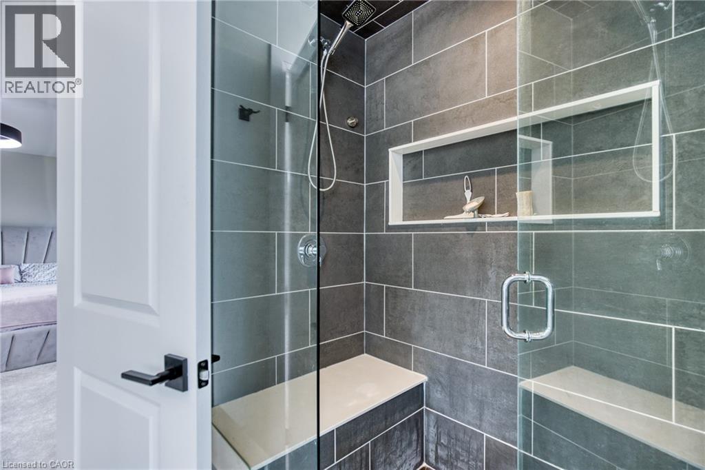 Modern shower enclosure featuring full-height grey tile, a built-in shower bench, a recessed niche, a handheld shower fixture, and a glass door - 71 Ian Ormston Drive, Kitchener, ON - Indoor Photo Showing Bathroom