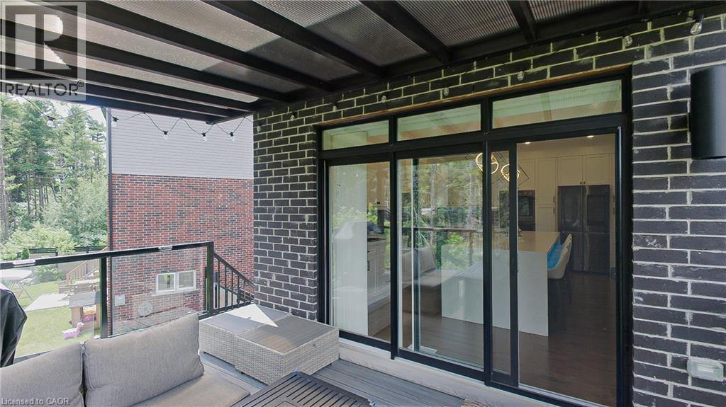 Covered outdoor patio with dark brick exterior and a clear glass railing - 71 Ian Ormston Drive, Kitchener, ON - Outdoor With Exterior