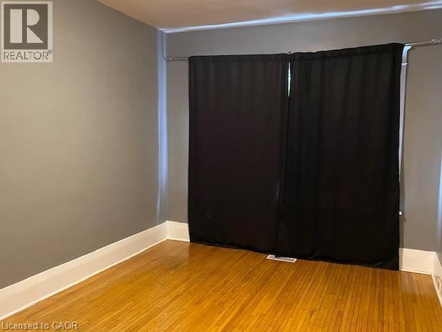 Room featuring wood flooring, neutral tone walls, white baseboards, and a window with dark curtains - 1066 Richmond Street, London, ON
