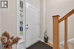 Bright entryway featuring a paneled door with polished hardware, a decorative glass sidelight, light wood-finish flooring, and a natural wood staircase railing -