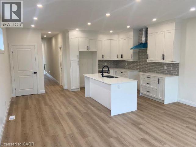 Bright kitchen featuring white shaker-style cabinetry, a central island with an undermount sink, quartz countertops, a subway tile backsplash, and recessed lighting - 48 Melbourne Street, Hamilton, ON - Indoor Photo Showing Kitchen With Double Sink