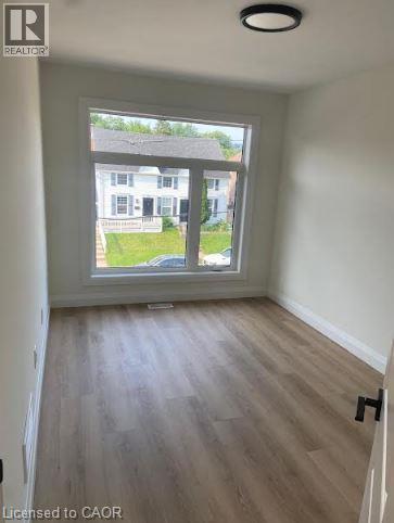 Room featuring a large picture window, wood-finish flooring, white baseboards, a flush-mount ceiling light, and a white interior door with a black handle - 48 Melbourne Street, Hamilton, ON - Indoor Photo Showing Other Room