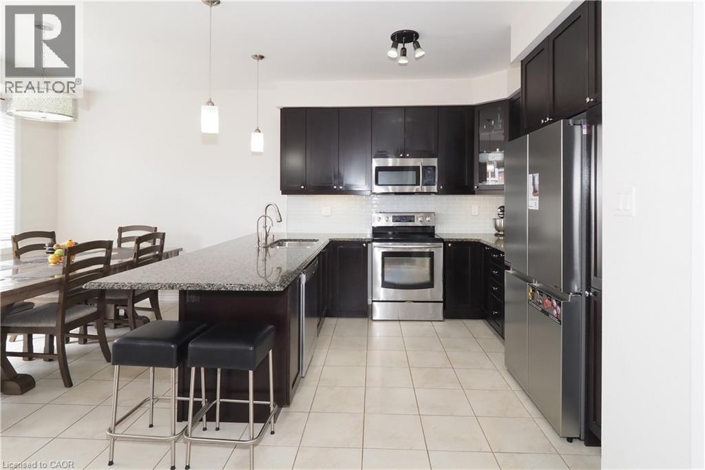 Open-concept kitchen featuring dark wood cabinetry, stainless steel appliances, a center island with a stone-finish countertop, and tile flooring - 213 Seabrook Drive, Kitchener, ON