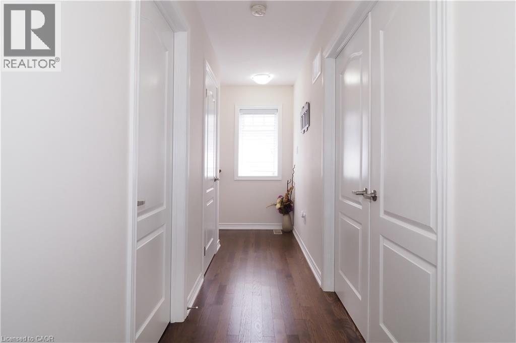 Hallway featuring dark wood-finish flooring, white paneled doors with brushed nickel hardware, and a window with horizontal blinds - 213 Seabrook Drive, Kitchener, ON