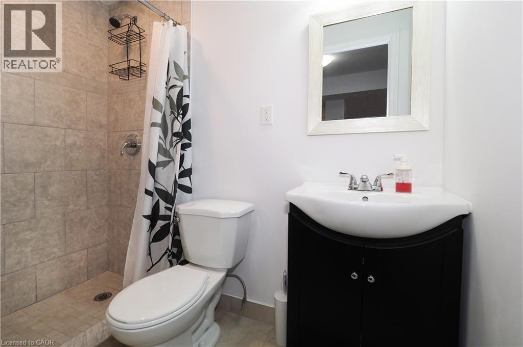 Bathroom featuring a tiled shower stall with chrome fixtures, a white toilet, and a black vanity with an integrated sink and chrome faucet - 213 Seabrook Drive, Kitchener, ON