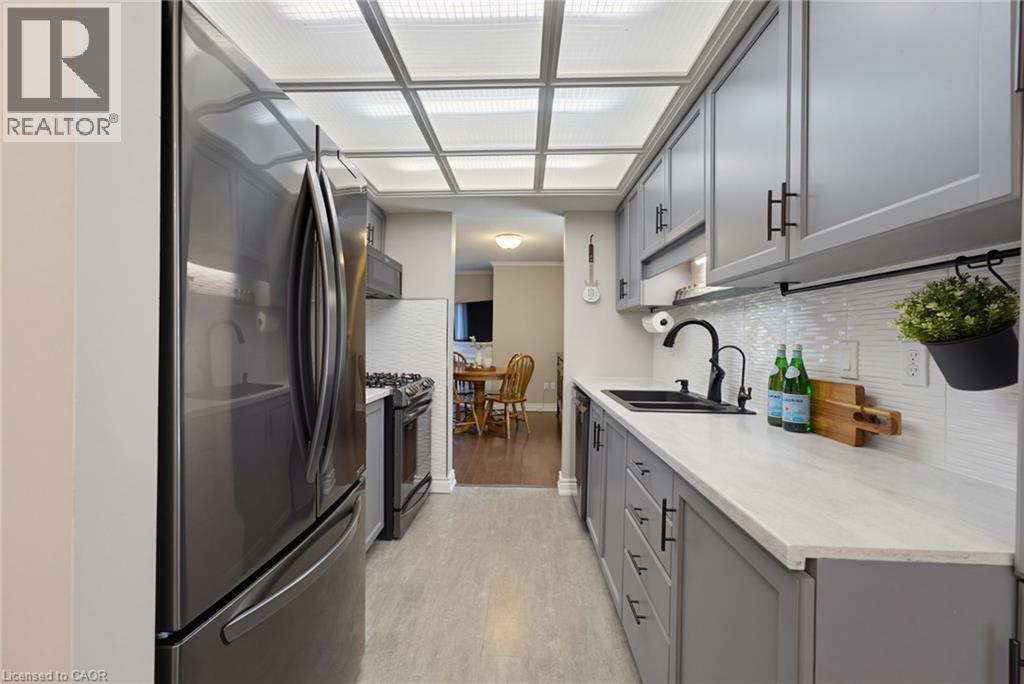 Galley kitchen featuring stainless steel appliances, light gray cabinetry with black hardware, white quartz-finish countertops, and a white tile backsplash - 520 Mayflower Street, Waterloo, ON - Indoor Photo Showing Kitchen With Double Sink With Upgraded Kitchen