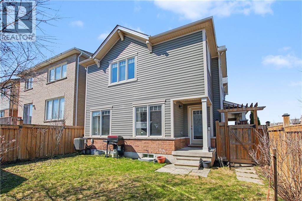 Rear exterior featuring gray horizontal siding, brick foundation, multiple windows, and a covered patio area with an exterior door - 60 Postmaster Drive, Kitchener, ON - Outdoor