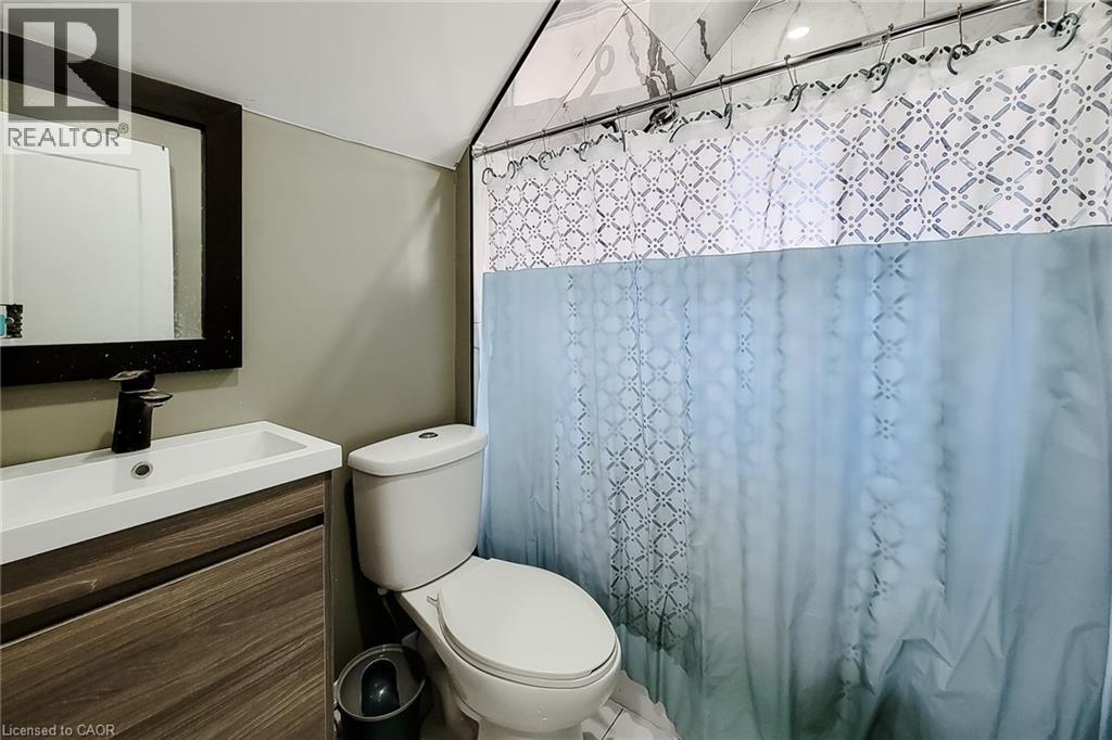 Bathroom featuring a wood-finish vanity with an integrated sink, a dark framed mirror, and matte black faucet - 334 Gage Avenue N, Hamilton, ON - Indoor Photo Showing Bathroom