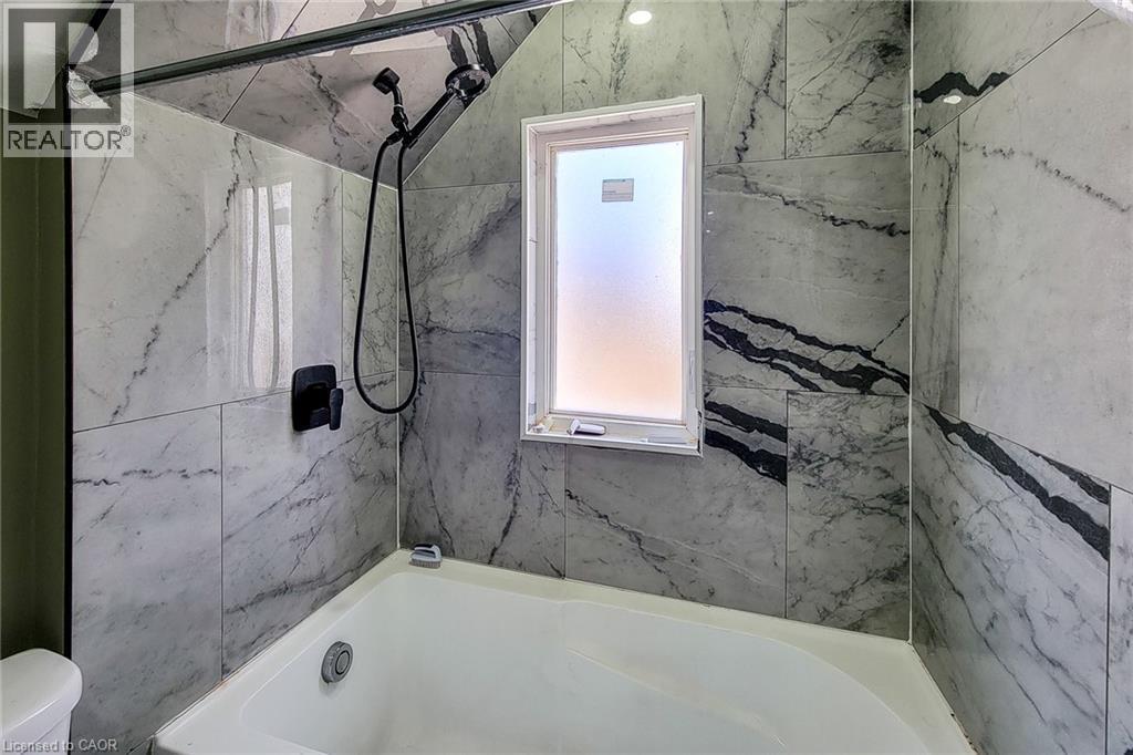 Bathtub and shower combination featuring floor-to-ceiling marbled tile, a frosted window, and matte black fixtures - 334 Gage Avenue N, Hamilton, ON - Indoor Photo Showing Bathroom