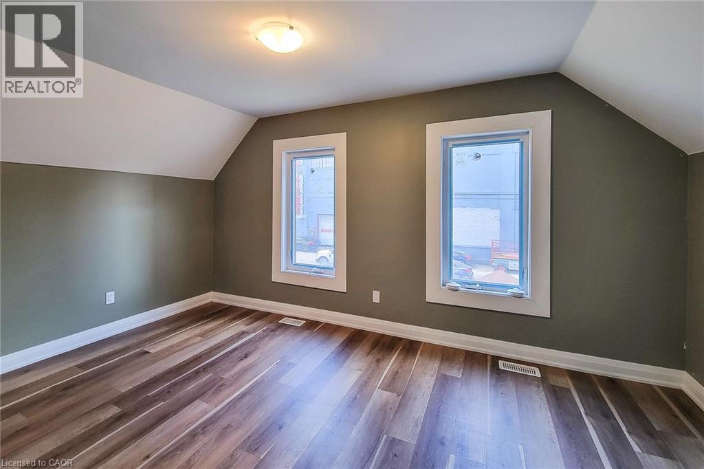 Room featuring wood-finish flooring, two windows with white trim, and a ceiling-mounted light fixture - 334 Gage Avenue N, Hamilton, ON - Indoor Photo Showing Other Room