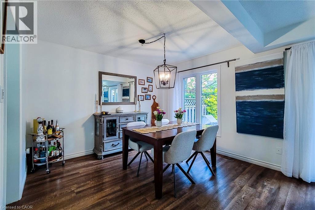 Dining area featuring wood-finish flooring, a contemporary chandelier, white walls, and a window providing natural light - 7 Davidson Boulevard Unit# 14, Dundas, ON - Indoor Photo Showing Dining Room